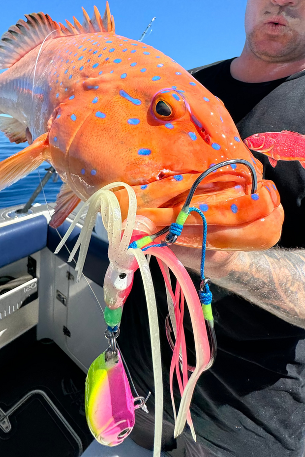 Man holding a large orange fish caught on a boat with a clear blue sky.